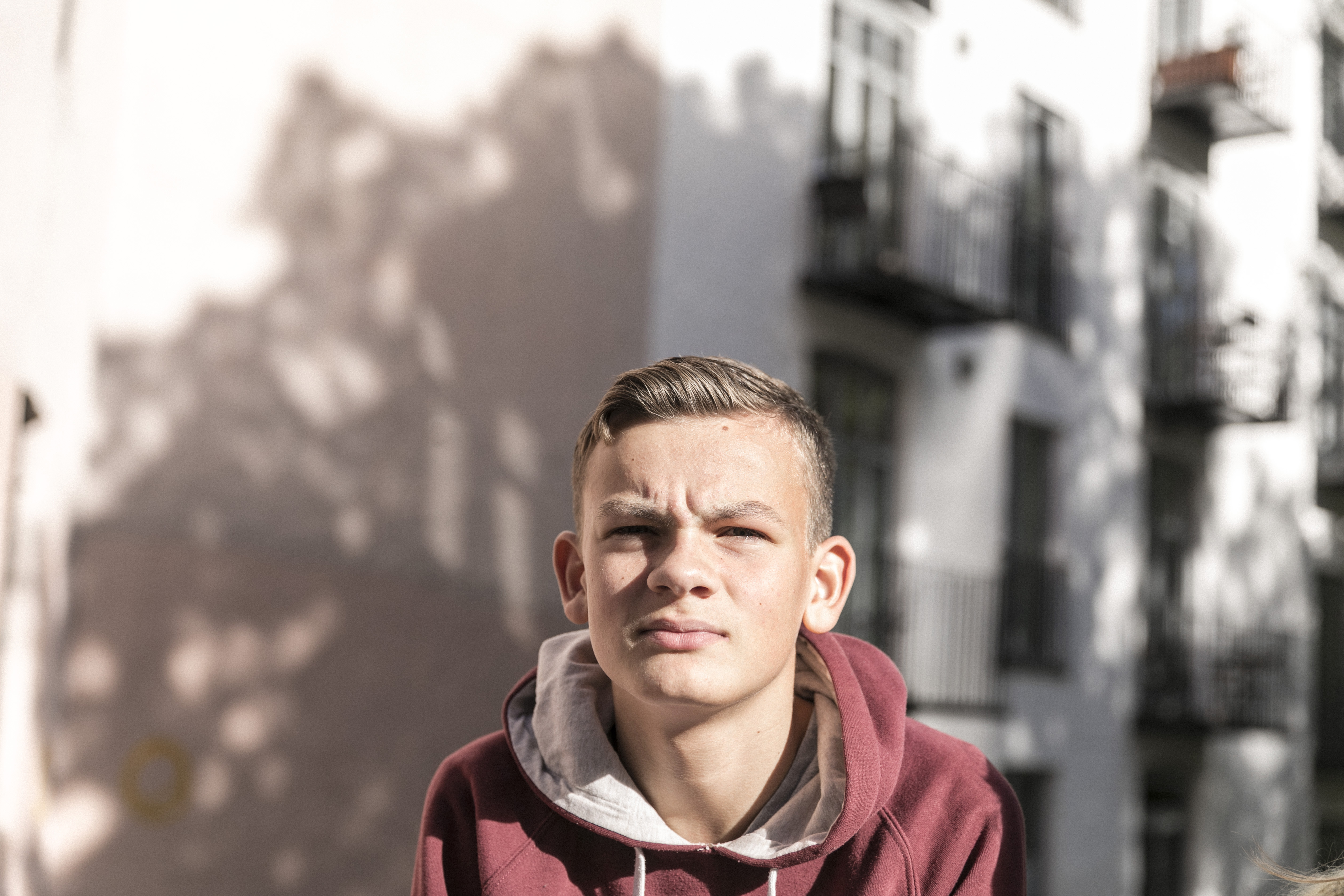 Tenåringsgutt med burguder hettejakke myser med øynene og ser avlorlig ut